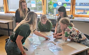 Rebecca Baumer (SCHUBZ) zeigt Patrizia Jäger (Lünestrom) und drei Kindern der IGS Lüneburg etwas auf den Arbeitsunterlagen.