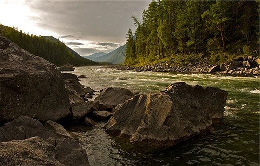 Ein Fluss mit großen Steinen in einer bergigen Landschaft.