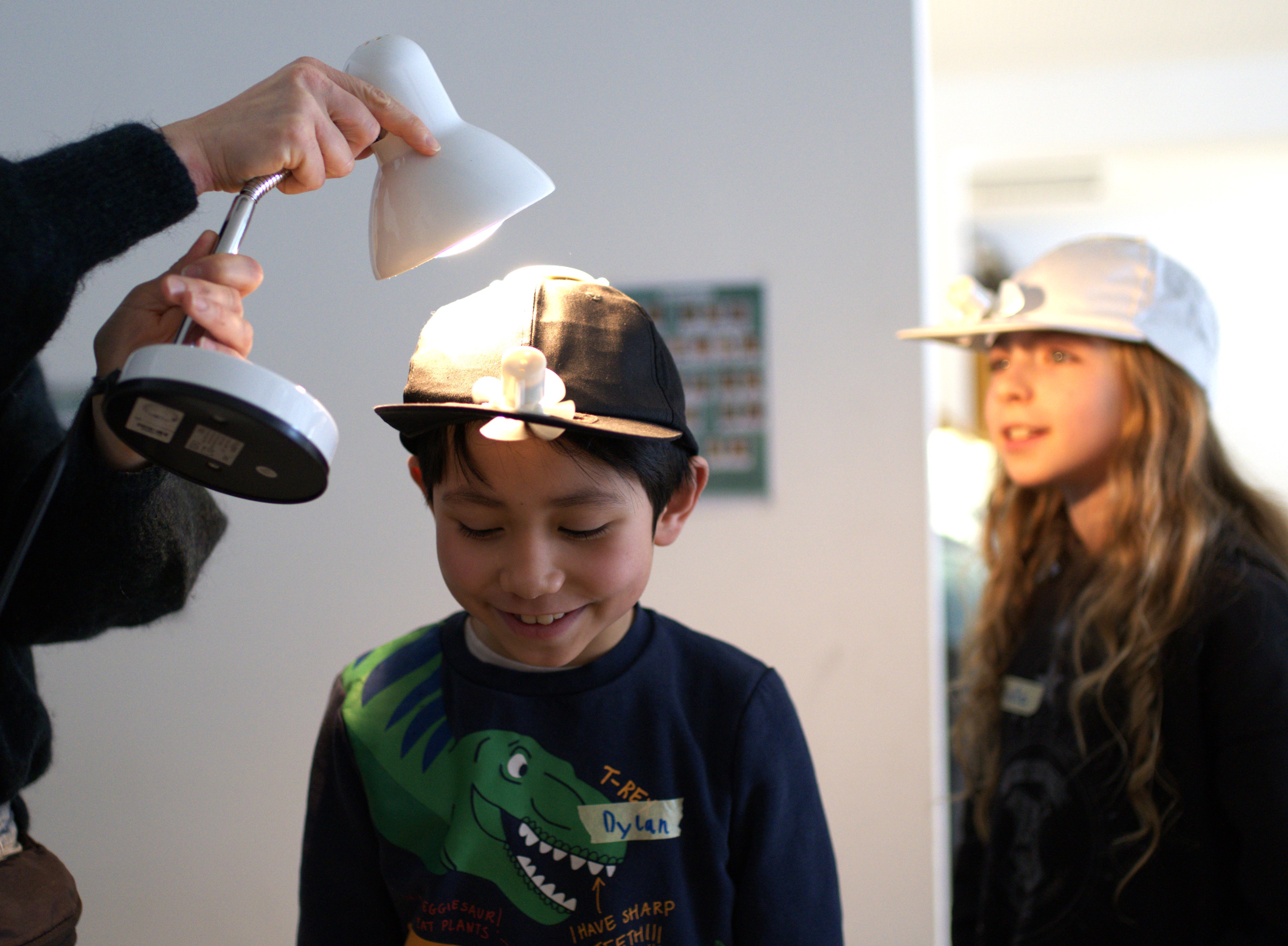 Mit einer Lampe wird der solarbetriebenen Ventilator an der Cap eines Schülers angetrieben.