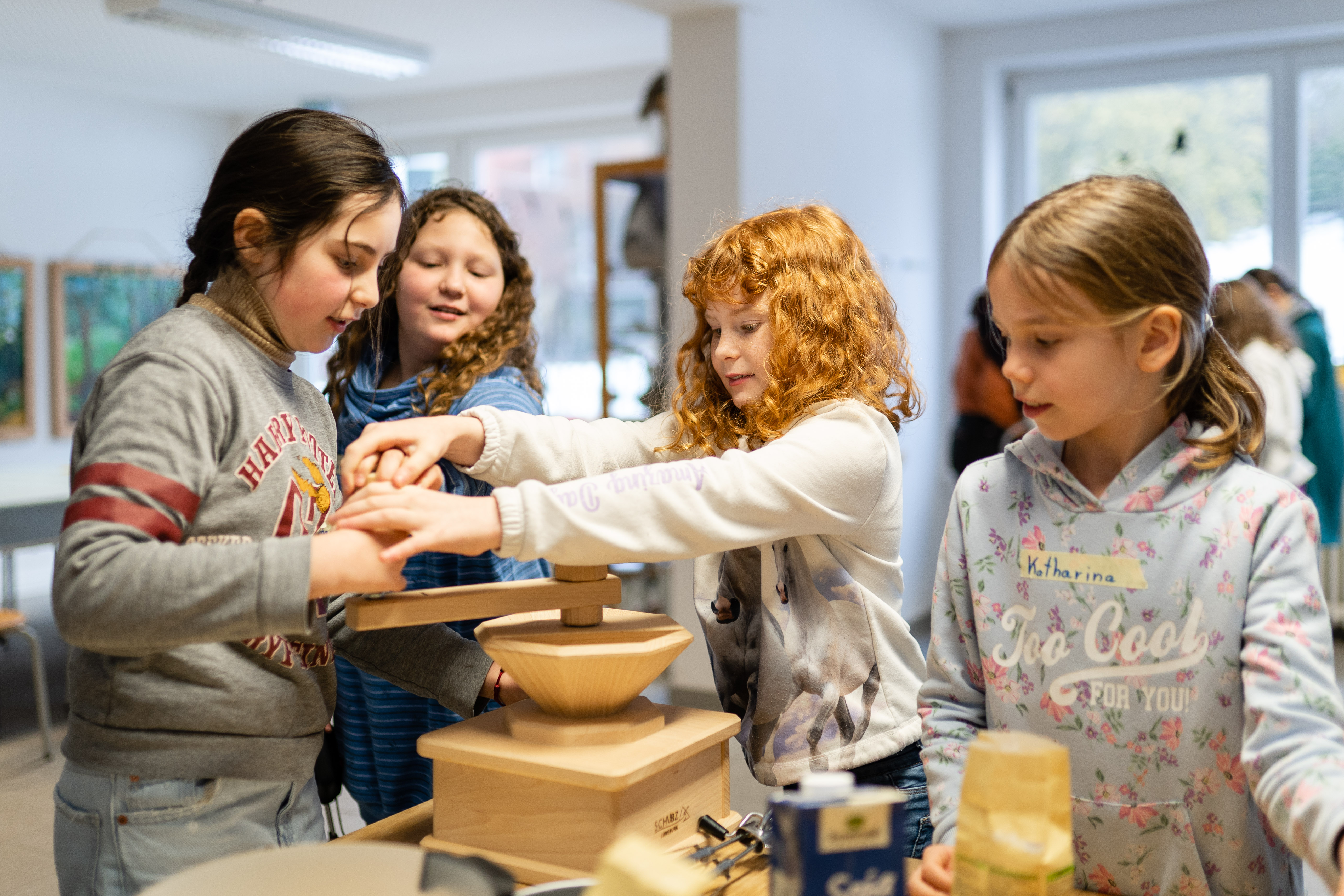 Mit einer handbetriebenen Mühle mahlen vier Schülerinnen Mehl.